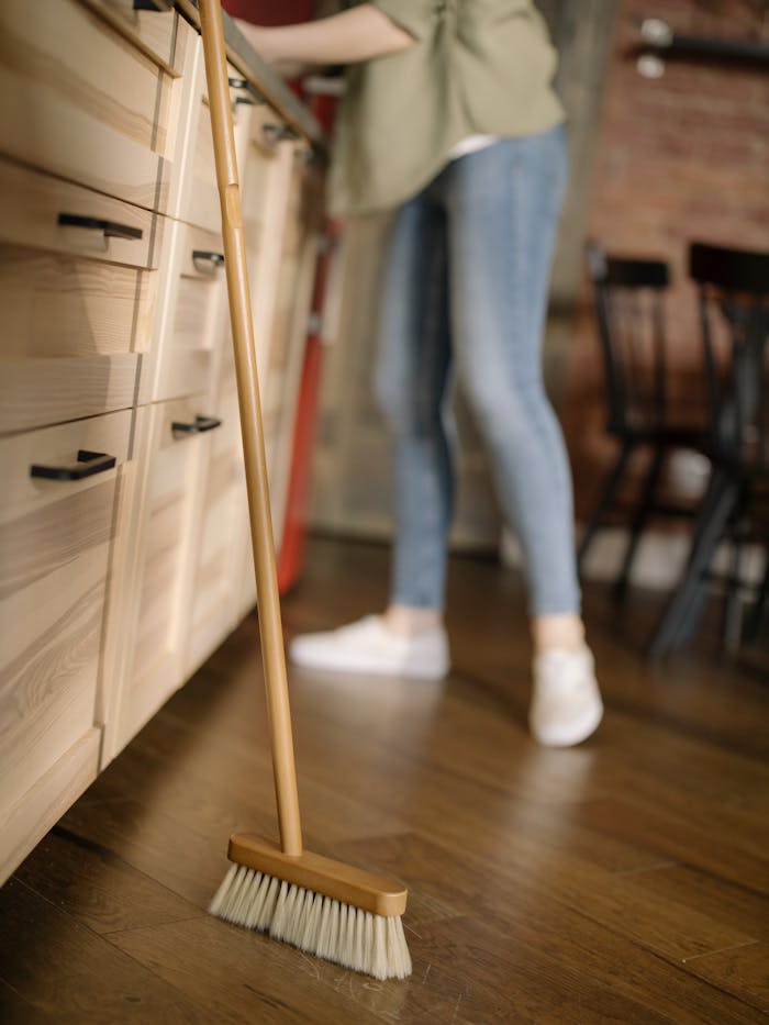 A woman in casual attire sweeps the kitchen floor, maintaining cleanliness in a cozy home.